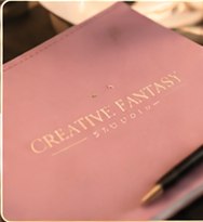 Agendă roz cu logoul Creative Fantasy Studio și un pix
